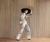 a woman in a hat and pants standing in front of a wooden wall