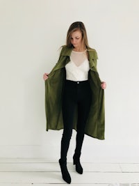 a woman wearing a green trench coat and black pants