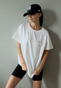 a woman in a white t - shirt and black shorts leaning against a wall