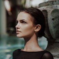 a woman is leaning against a stone wall near a pool