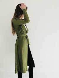 a woman wearing a green trench coat and black leggings