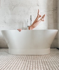 a woman's legs in a white bathtub on a tiled floor