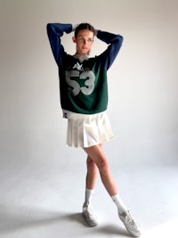 a woman is posing in a white skirt and a green sweatshirt