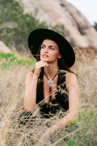a woman in a black hat sitting in tall grass