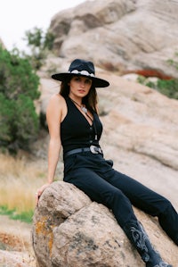 a woman in a black hat sitting on a rock